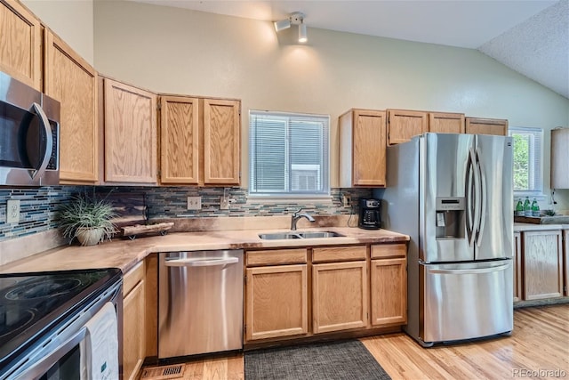 kitchen with lofted ceiling, stainless steel appliances, decorative backsplash, sink, and light hardwood / wood-style floors