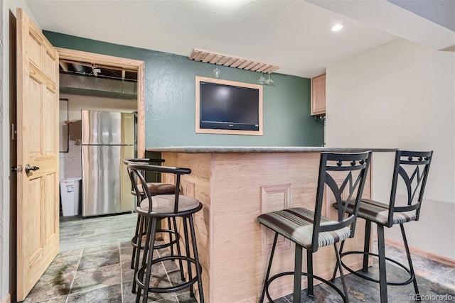 bar featuring light brown cabinetry and stainless steel refrigerator