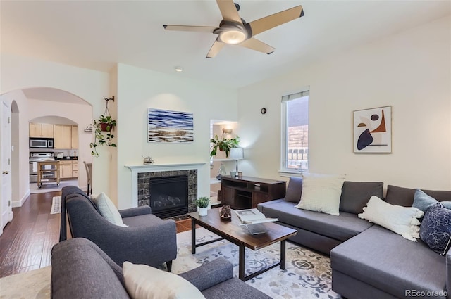 living room featuring baseboards, arched walkways, ceiling fan, dark wood-type flooring, and a fireplace