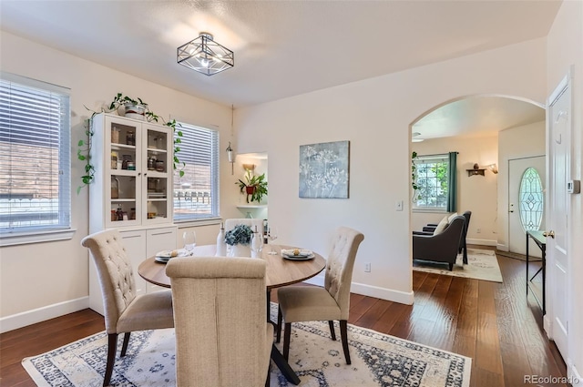 dining room featuring arched walkways, dark wood-style flooring, and baseboards