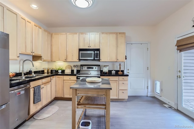 kitchen with stainless steel appliances, light brown cabinetry, dark countertops, and a sink