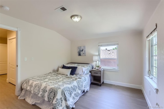 bedroom featuring lofted ceiling, visible vents, baseboards, and wood finished floors