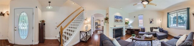 foyer entrance with baseboards, a ceiling fan, a glass covered fireplace, stairway, and wood finished floors