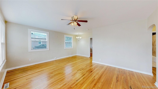 empty room featuring arched walkways, light wood-style flooring, visible vents, and ceiling fan with notable chandelier