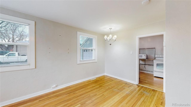 unfurnished dining area featuring baseboards, light wood-style floors, and a notable chandelier
