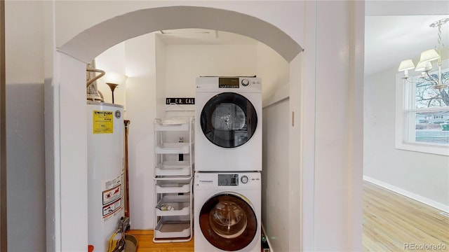 laundry room featuring water heater, stacked washer / drying machine, light wood-type flooring, laundry area, and arched walkways