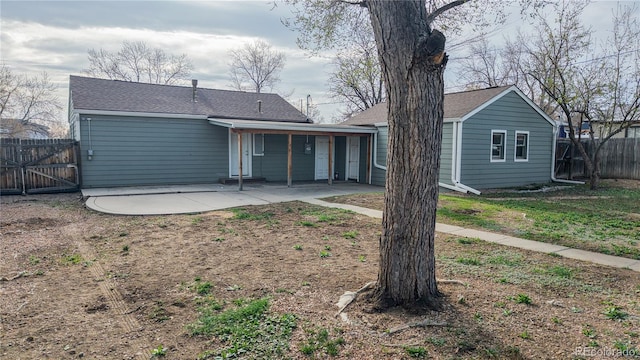 back of property featuring a shingled roof, fence, and a patio