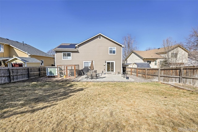 rear view of house featuring a patio area, a fenced backyard, a lawn, and roof mounted solar panels