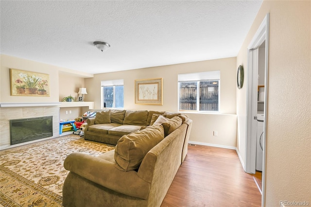 living room with a textured ceiling, wood finished floors, baseboards, and a tile fireplace