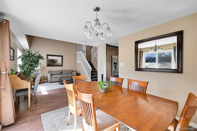 dining space featuring light wood finished floors, a textured ceiling, stairs, and an inviting chandelier