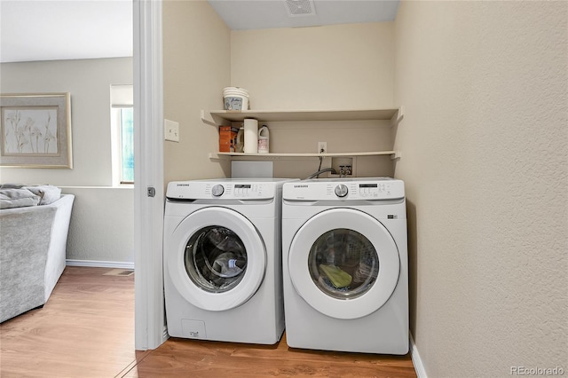 laundry area featuring light wood finished floors, baseboards, laundry area, a textured wall, and separate washer and dryer