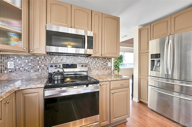 kitchen with backsplash, glass insert cabinets, light stone countertops, light wood-style floors, and stainless steel appliances