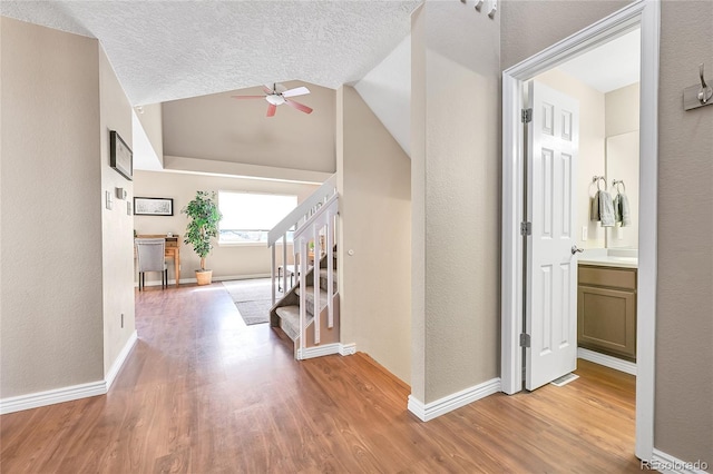 corridor with stairway, baseboards, light wood finished floors, lofted ceiling, and a textured ceiling