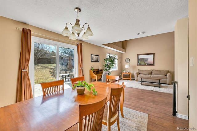 dining area with a notable chandelier, a textured ceiling, baseboards, and wood finished floors