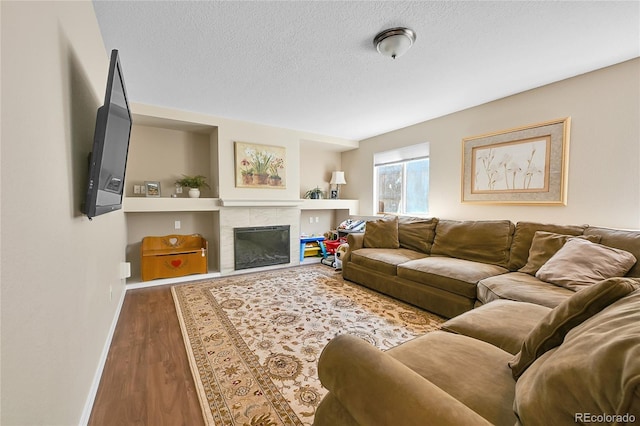 living room featuring a tile fireplace, a textured ceiling, baseboards, and wood finished floors