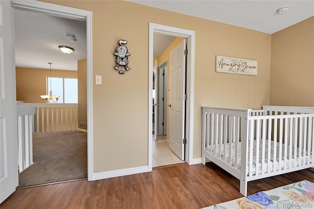 bedroom featuring a crib, a notable chandelier, wood finished floors, and baseboards