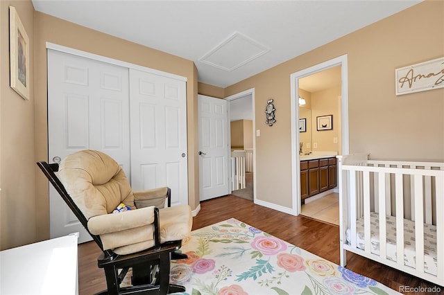 bedroom with baseboards, attic access, wood finished floors, a closet, and a nursery area