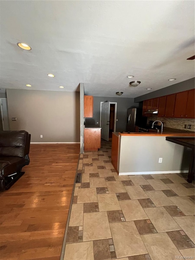 kitchen featuring sink, kitchen peninsula, stainless steel fridge, decorative backsplash, and light wood-type flooring