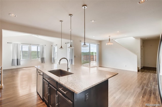 kitchen with a center island with sink, decorative light fixtures, light stone countertops, stainless steel dishwasher, and sink