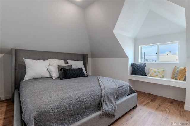 bedroom with vaulted ceiling, wood finished floors, and baseboards