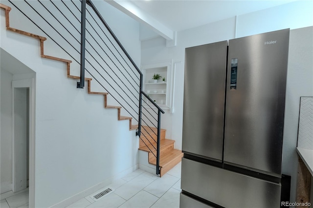 interior space with light tile patterned floors, baseboards, visible vents, freestanding refrigerator, and beam ceiling