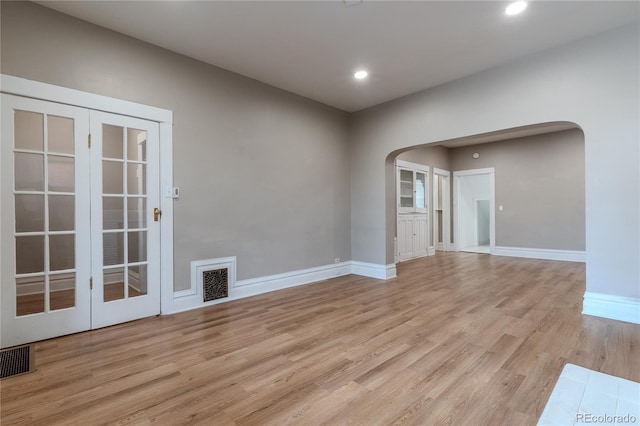 empty room featuring light wood-type flooring, visible vents, arched walkways, and baseboards