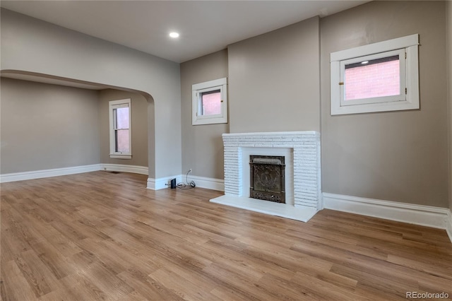 unfurnished living room featuring arched walkways, a fireplace, light wood finished floors, recessed lighting, and baseboards