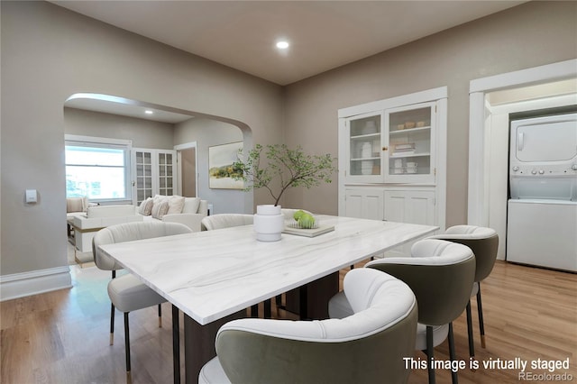 dining room with arched walkways, recessed lighting, baseboards, stacked washer / drying machine, and light wood finished floors