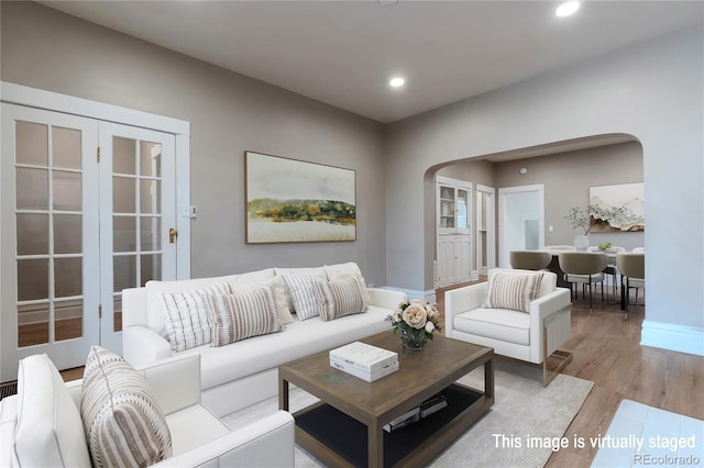 living room featuring arched walkways, baseboards, light wood-style flooring, and recessed lighting