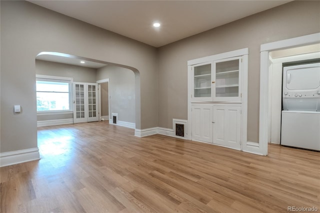 interior space featuring light wood finished floors, baseboards, visible vents, arched walkways, and stacked washer and clothes dryer