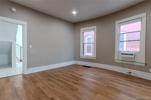 empty room featuring cooling unit, visible vents, light wood-type flooring, baseboards, and stairs