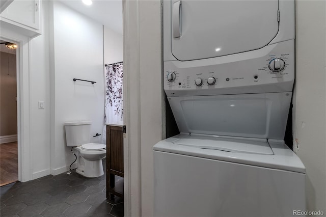 clothes washing area with laundry area, dark tile patterned floors, stacked washing maching and dryer, and baseboards