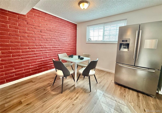 dining space featuring light wood finished floors, brick wall, baseboards, and a textured ceiling