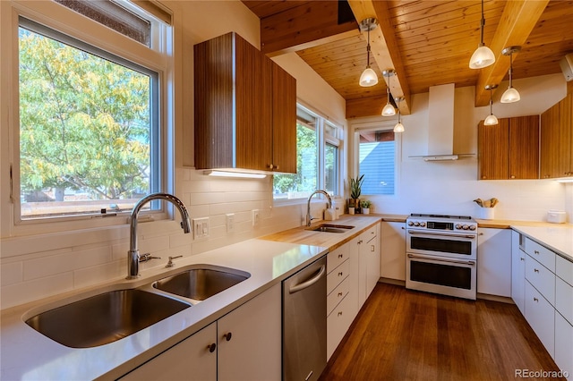 kitchen with white cabinets, sink, wall chimney range hood, appliances with stainless steel finishes, and decorative light fixtures