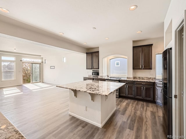 kitchen with a center island, dark wood-type flooring, a kitchen breakfast bar, stainless steel fridge, and light stone countertops