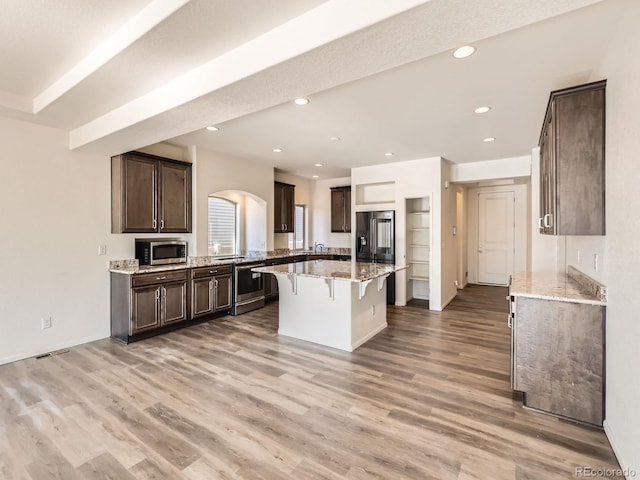 kitchen featuring dark brown cabinetry, a kitchen breakfast bar, appliances with stainless steel finishes, a kitchen island, and hardwood / wood-style flooring