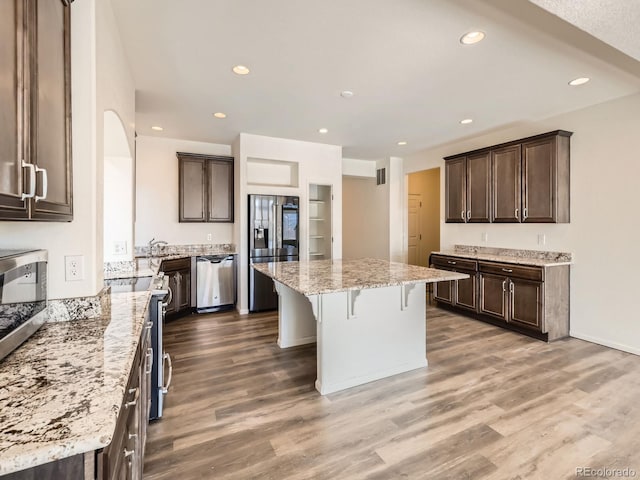 kitchen with appliances with stainless steel finishes, light stone counters, dark brown cabinets, hardwood / wood-style flooring, and a kitchen island