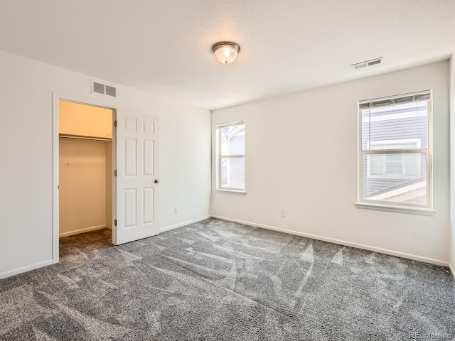 unfurnished bedroom with dark carpet, a walk in closet, and a closet