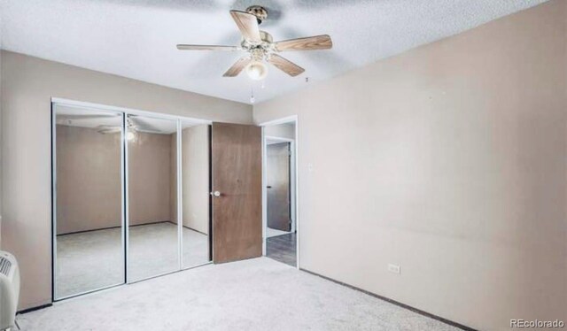 unfurnished bedroom featuring ceiling fan, a textured ceiling, light colored carpet, and a closet