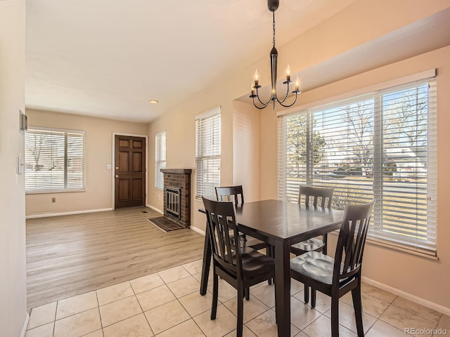 dining space featuring a chandelier, light tile patterned floors, a fireplace, and baseboards