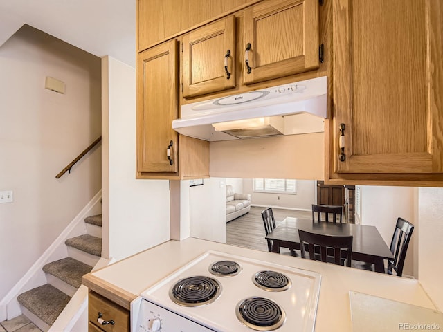 kitchen with brown cabinets, white electric range, light countertops, under cabinet range hood, and baseboards