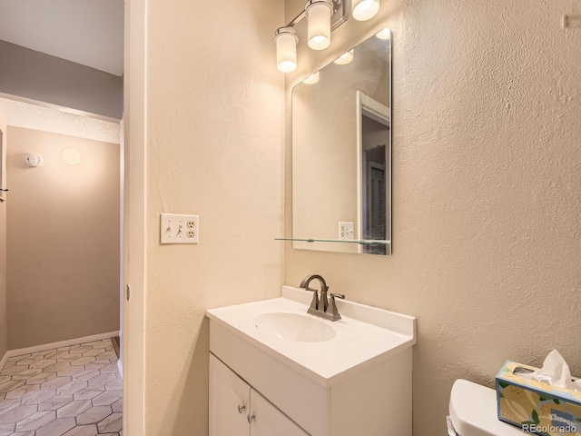 half bathroom featuring toilet, tile patterned floors, a textured wall, and vanity