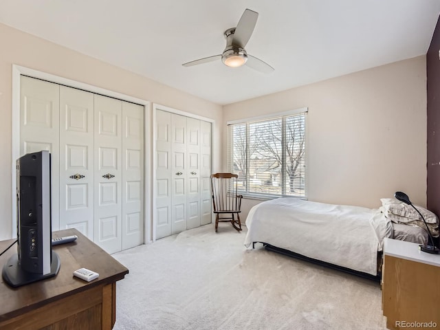 bedroom with a ceiling fan, multiple closets, and light colored carpet