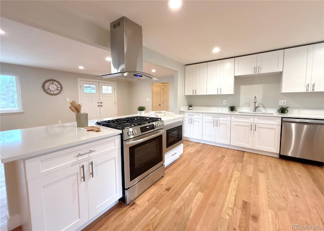 kitchen featuring light wood-style flooring, island range hood, a sink, light countertops, and appliances with stainless steel finishes