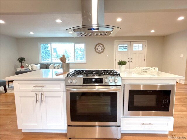 kitchen featuring white cabinets, gas stove, island exhaust hood, built in microwave, and recessed lighting