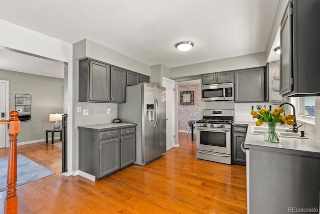 kitchen with light wood-style flooring, gray cabinets, a sink, stainless steel appliances, and light countertops