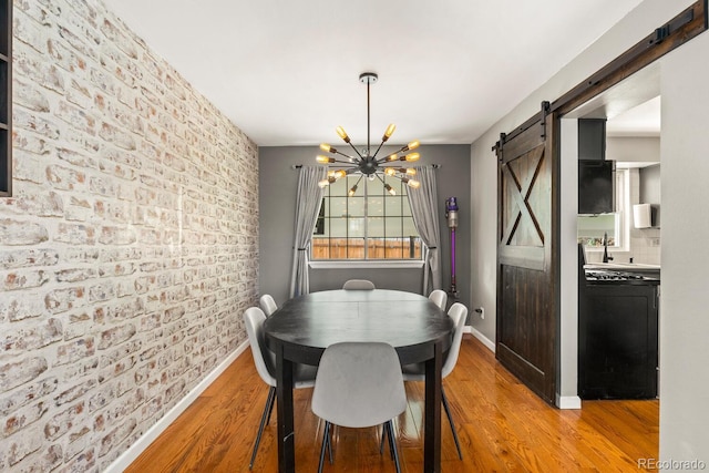 dining space featuring brick wall, baseboards, a barn door, and wood finished floors