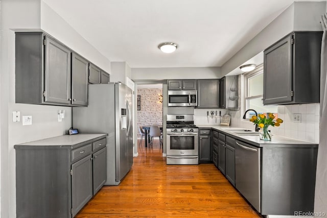 kitchen with light countertops, decorative backsplash, appliances with stainless steel finishes, wood finished floors, and a sink