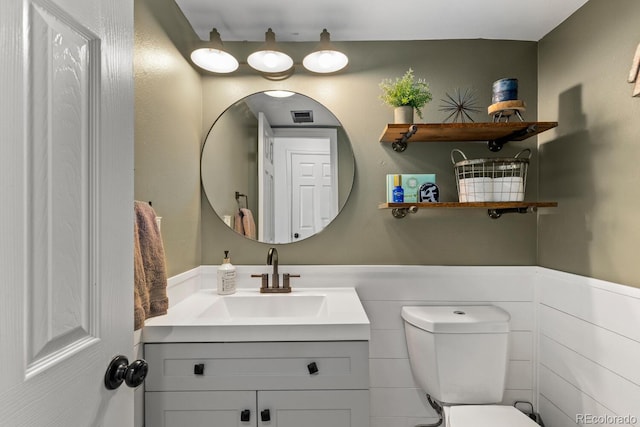 half bath featuring a wainscoted wall, toilet, vanity, and visible vents