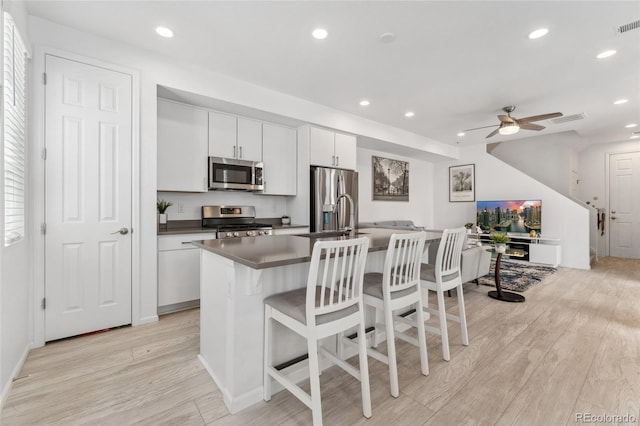 kitchen featuring dark countertops, stainless steel appliances, a kitchen breakfast bar, a kitchen island with sink, and light wood-type flooring